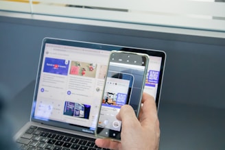 a person holding a cell phone and a laptop