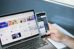 a man holding two cell phones next to a laptop