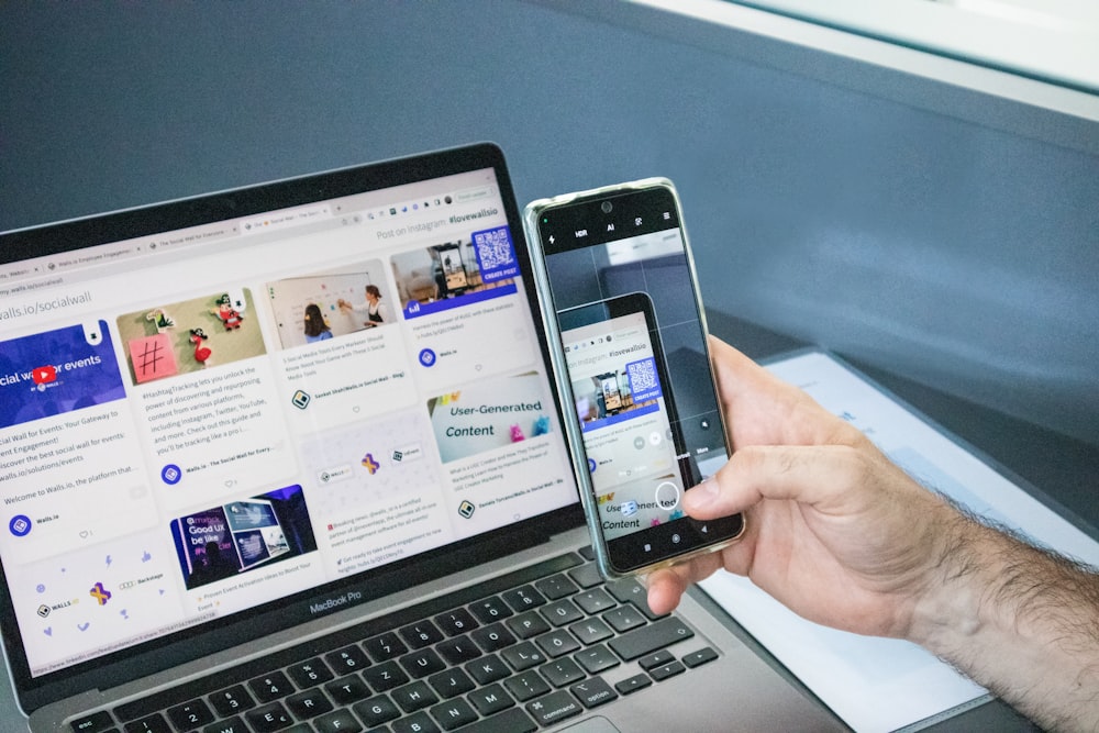 a man holding two cell phones next to a laptop