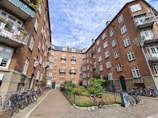 Sunlit communal courtyard with benches and greenery between residential buildings.
