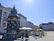 An ornate kiosk with a decorative roof, surrounded by a cobblestone plaza. The kiosk offers services like Segway tours and draft beer to go. Outdoor seating with tables and umbrellas is visible, alongside a street lined with historical buildings under a clear blue sky.