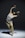 A person appears to be performing a contemporary dance move, captured mid-motion while bending backwards with arms raised expressively. The dance is performed on a bare stage with a plain, softly lit background.