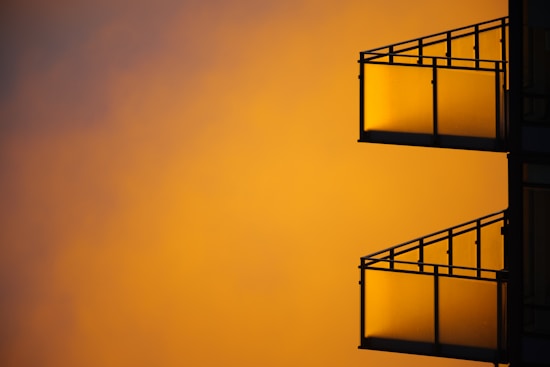 Silhouetted view of two balconies with metal railings against a vibrant, warm sunset sky.