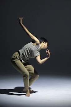 A graceful dancer captured mid-leap in a softly lit studio with minimalist beige and dark gray tones.
