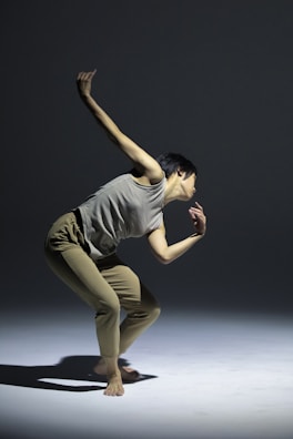 A person is captured in a dynamic dance pose, balancing gracefully on one foot. The scene is set against a minimalist backdrop with soft lighting casting shadows on the floor.