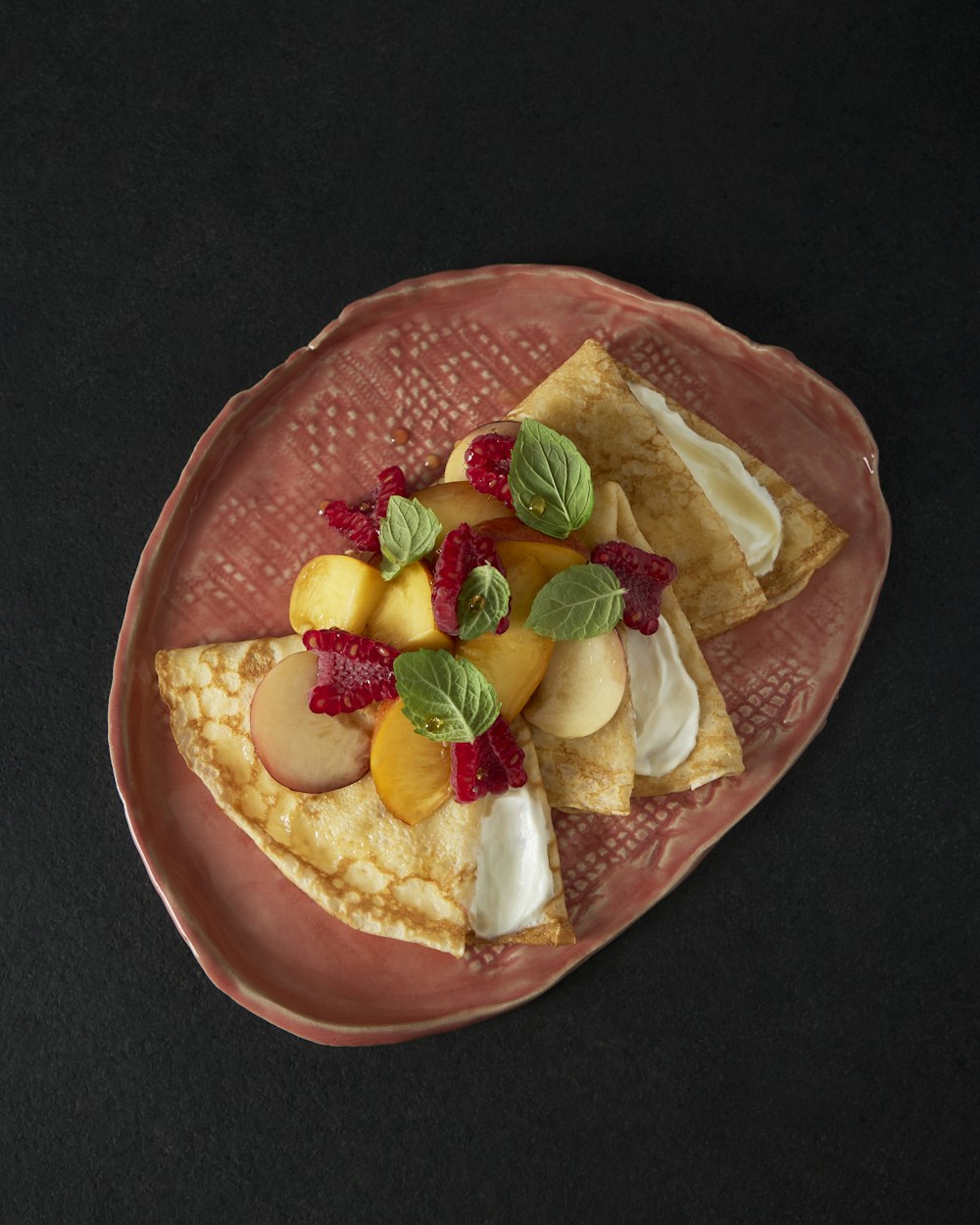 a pink plate topped with a slice of pie covered in fruit