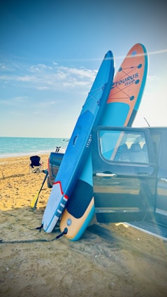 A portable inflatable surfboard being packed into a travel bag near a beachside vacation spot