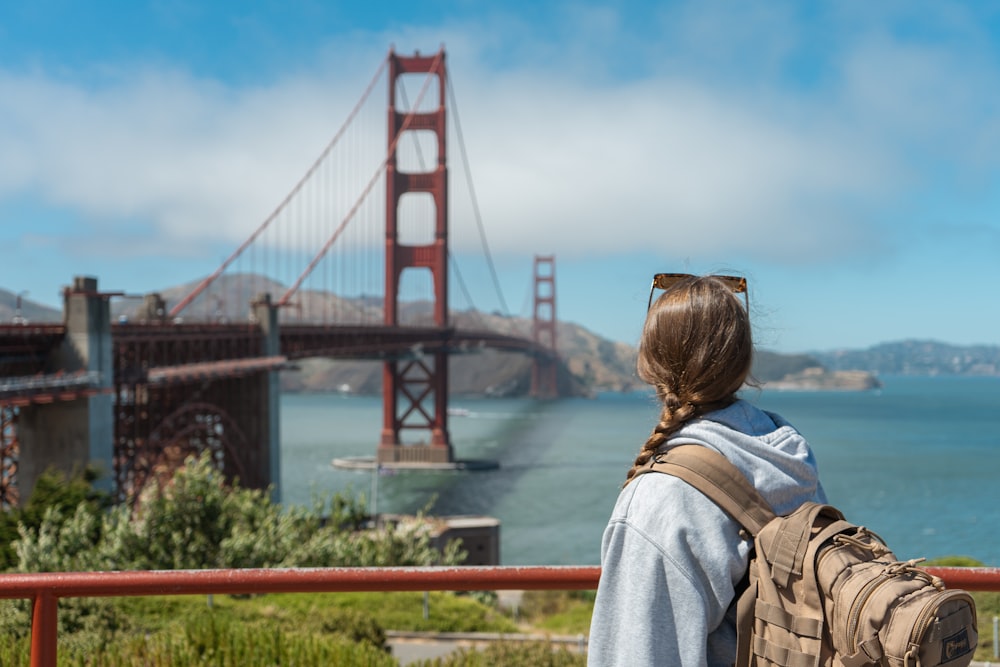 a woman with a backpack looking at the golden gate bridge