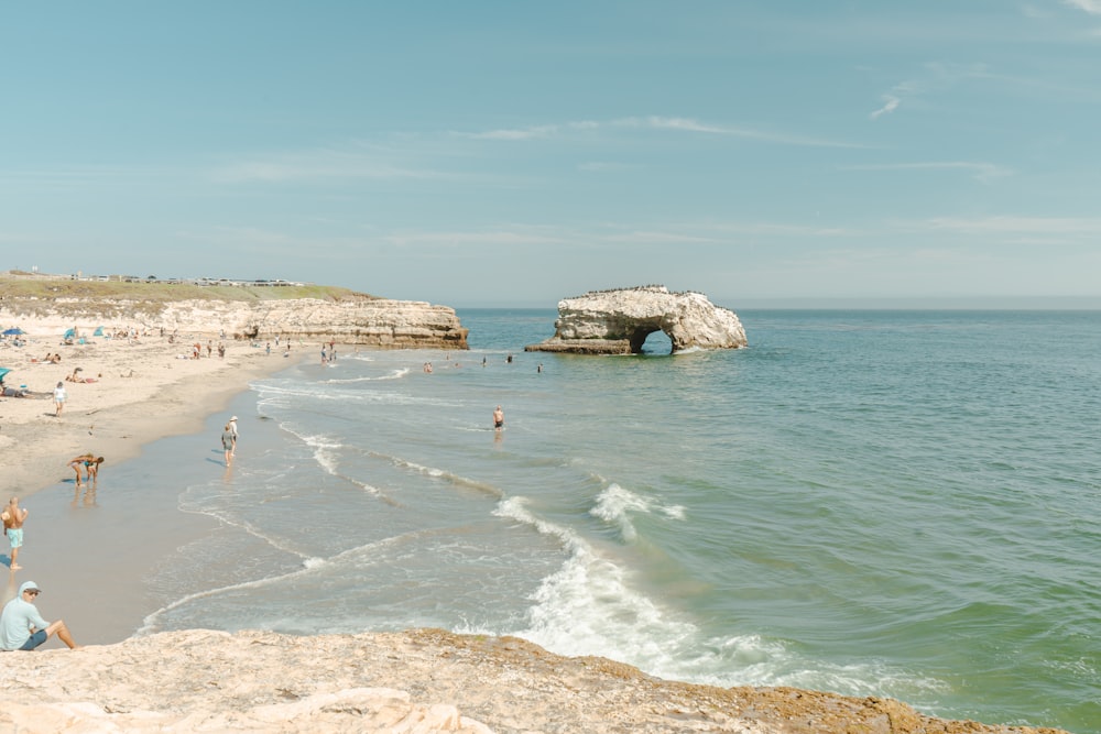 a beach with people on it and a rock formation in the water