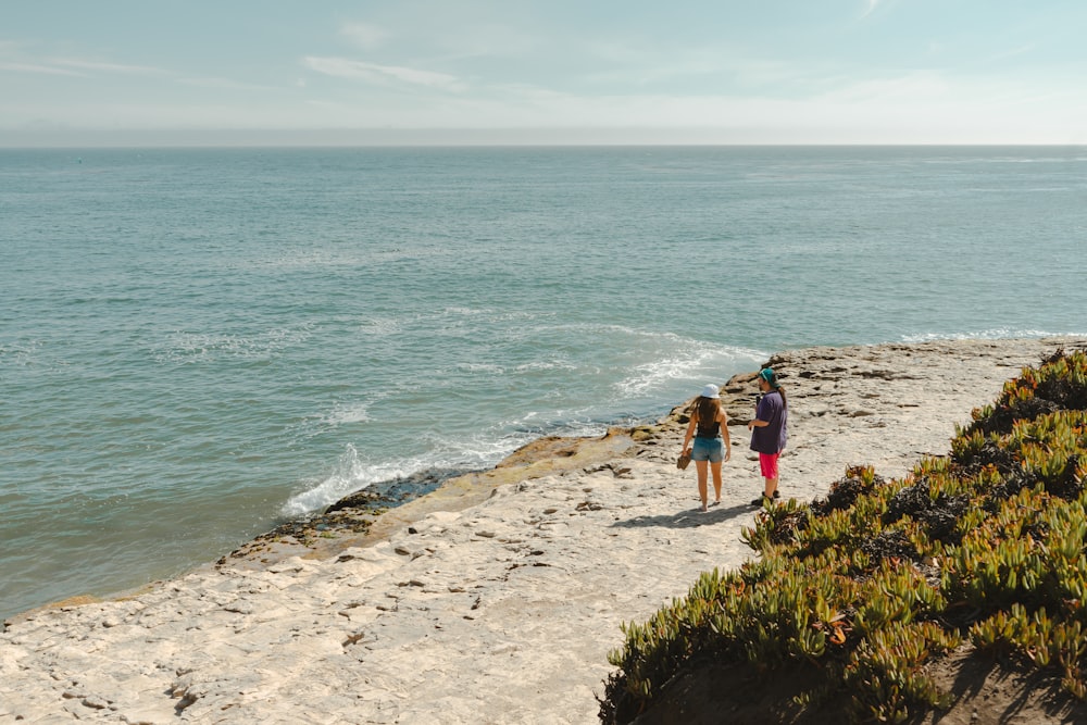 a couple of people standing on top of a sandy beach