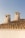 Two rustic chimneys are perched on a traditional terracotta-tiled roof against a clear blue sky. The chimneys are made of a rough, beige stone that gives an aged appearance.