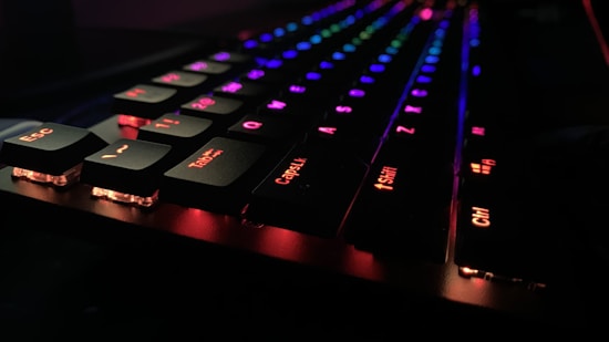 A close-up of a mechanical keyboard with backlit keys glowing in vibrant colors, including red, blue, and green. The keys are raised and appear to be illuminated in a dark setting, creating a striking contrast.