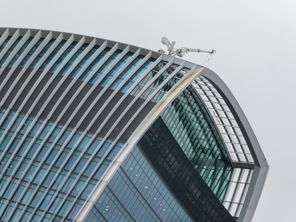 A modern skyscraper featuring a unique curved design with a series of horizontal and vertical lines creating a grid pattern. The building has a glass facade and a construction crane visible at the top.