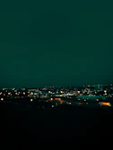 Nighttime view of a truck convoy moving along a highway under city lights.