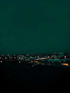Nighttime view of a truck convoy moving along a highway under city lights.