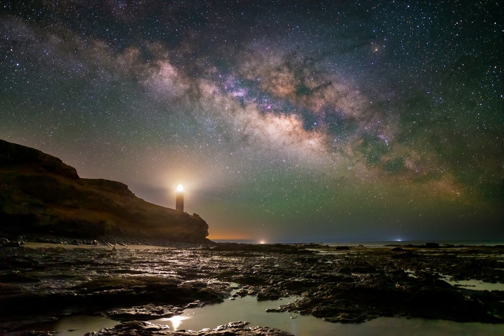 a lighthouse on a rocky shore under a night sky filled with stars