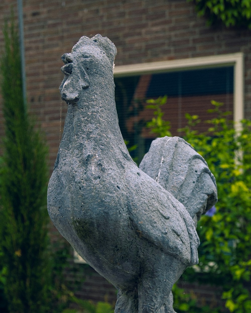 Statue eines Hahns vor einem Backsteingebäude