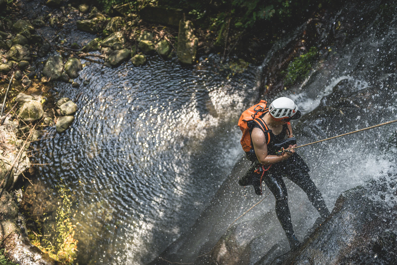 Canyoneer wearing a helmet rappelling down a waterfall on a rope