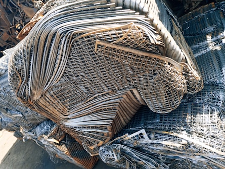 A large pile of intricately layered metal grids and sheets, likely indicating a scrap or recycling yard. The metal consists of various shades of gray, silver, and rusted brown, showing signs of weathering and age.