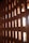 A textured wall made of interlocking reddish-brown bricks with openings allowing light to pass through. The bricks are arranged in a geometric pattern, creating a play of light and shadows.