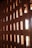 A textured wall made of interlocking reddish-brown bricks with openings allowing light to pass through. The bricks are arranged in a geometric pattern, creating a play of light and shadows.