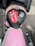 A motorcycle seat cover features a prominent red and white logo of a tongue and lips, the phrase 'ROCK N ROLL,' and an illustration of an eagle wearing sunglasses. The seat sits atop a pink motorcycle with chrome handlebars, parked on an asphalt surface.