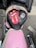 A motorcycle seat cover features a prominent red and white logo of a tongue and lips, the phrase 'ROCK N ROLL,' and an illustration of an eagle wearing sunglasses. The seat sits atop a pink motorcycle with chrome handlebars, parked on an asphalt surface.