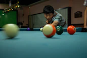 A smiling student watching an online billiards lesson on a tablet while practicing shots.