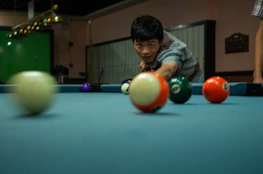 A smiling student watching an online billiards lesson on a tablet while practicing shots.