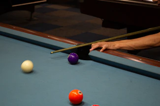 A close-up of a hand holding a sleek pool cue stick over a green felt pool table.