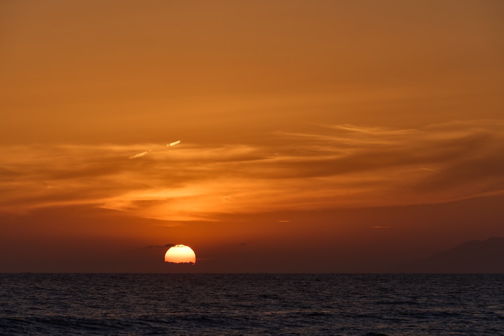 the sun is setting over the ocean with clouds