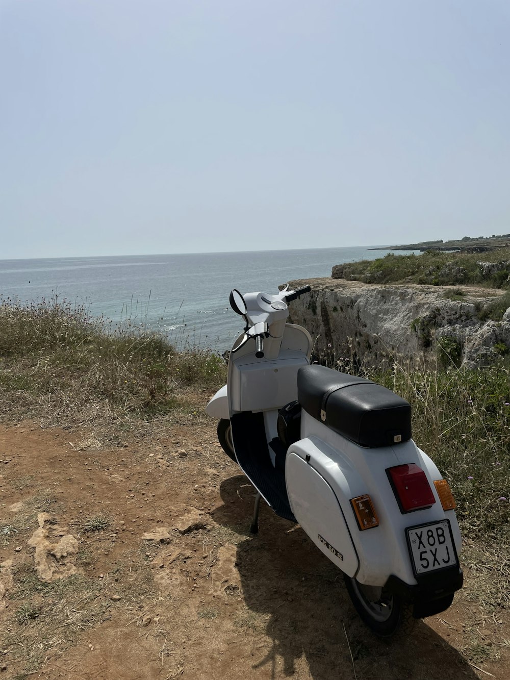 a scooter parked on the side of a dirt road near the ocean