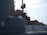 A detailed view of a naval vessel, featuring large metal structures and various deck equipment. The ship has a number 9 marked on its side, and there are ropes and other nautical elements visible. The lighting suggests a calm, possibly overcast day.