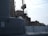 A detailed view of a naval vessel, featuring large metal structures and various deck equipment. The ship has a number 9 marked on its side, and there are ropes and other nautical elements visible. The lighting suggests a calm, possibly overcast day.