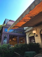 Wide shot of the storefront of the boulangerie with warm light glowing inside at dawn.