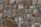 A wall constructed from an assortment of irregularly shaped stones in various earthy tones, including brown, gray, and beige. The stones are held together with mortar, creating a rustic and textured appearance.