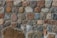 A wall constructed from an assortment of irregularly shaped stones in various earthy tones, including brown, gray, and beige. The stones are held together with mortar, creating a rustic and textured appearance.
