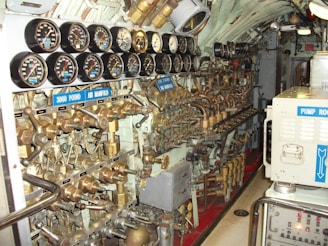A complex array of gauges, valves, and pipes fills the submarine's control room. The dials display various pressure readings, and the intricate arrangement of brass machinery suggests a highly technical environment. Labels such as '3000 Pound Air Manifold' and 'Pump Room' indicate the functionality related to air and pumps.