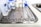 A stainless steel tray is arranged with various surgical instruments and medical supplies. There are pairs of scissors, forceps, and a pair of tweezers. In the background, there are bottles of antiseptic solution and medical tape.