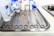 A stainless steel tray is arranged with various surgical instruments and medical supplies. There are pairs of scissors, forceps, and a pair of tweezers. In the background, there are bottles of antiseptic solution and medical tape.
