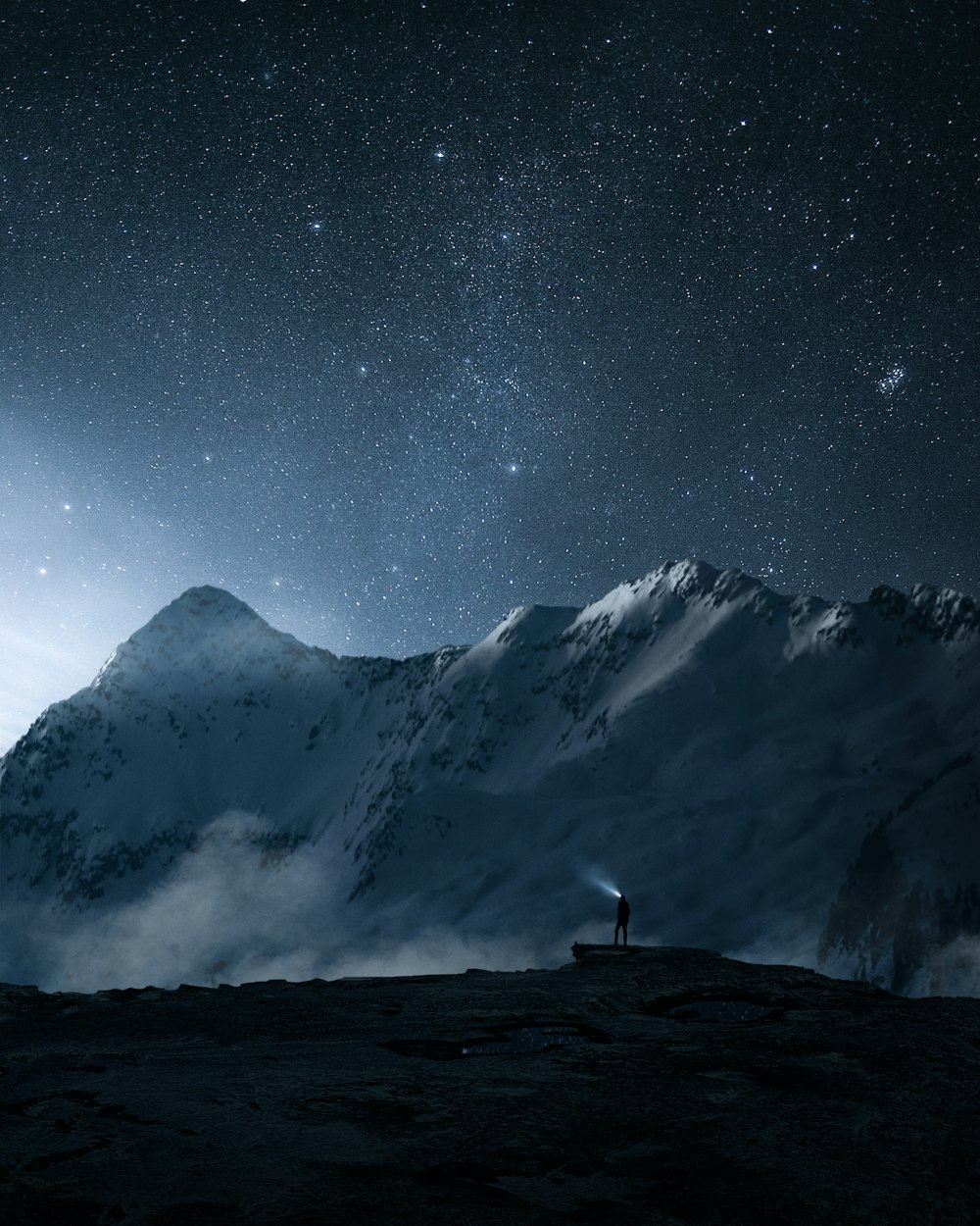 a man standing on top of a snow covered mountain under a night sky