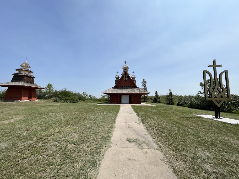 a grassy field with a path leading to two buildings