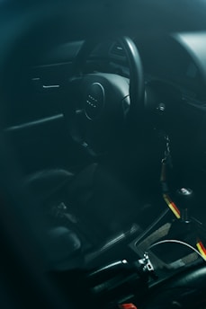 The interior of a car featuring a steering wheel with a logo in the center. The gear shift is visible, alongside a keychain hanging from the ignition. The seats and the console area have a dark, sleek appearance.