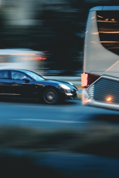 A motion blur effect captures a black car speeding past a large white bus on a city street. The background appears dark, with lights from other vehicles creating streaks, conveying a sense of movement and urgency.