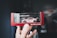 A hand is holding a boxed model car with a pink color and racing decals. The model car is enclosed in a display case with a red border featuring the text 'ignition.model.' The background is blurred, drawing focus to the detailed toy car.