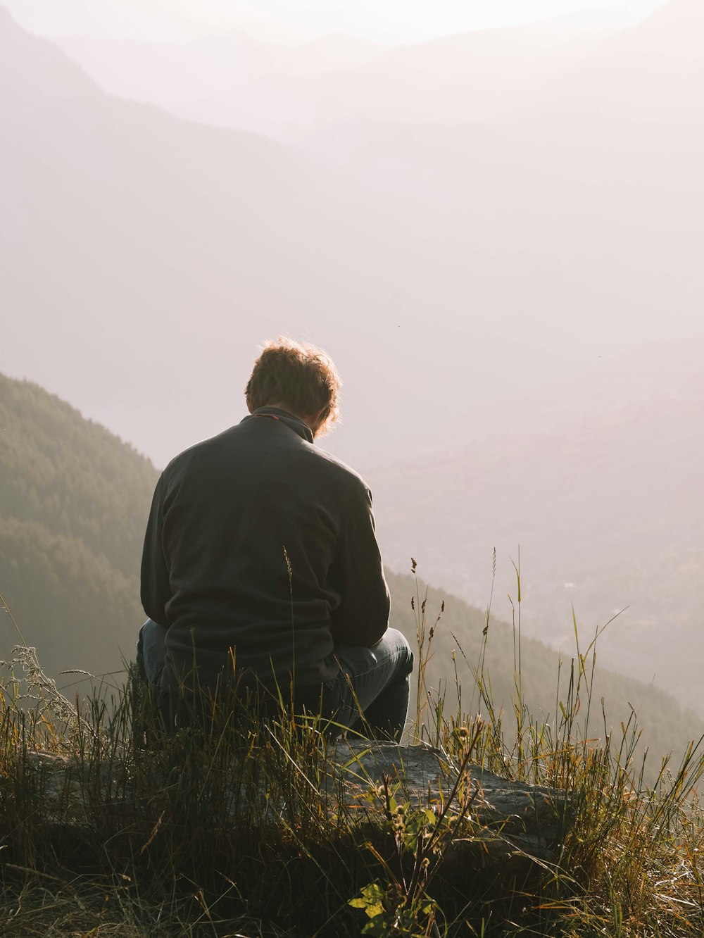 a man sitting on top of a hill overlooking a valley