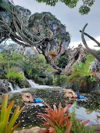 A lush, fantastical landscape with intricate, floating rock formations covered in dense foliage and vines. Below, there is a serene waterway with small waterfalls and vibrant, unusual plants, including striking blue and orange foliage. The scene evokes a sense of otherworldly beauty and tranquil mystery.