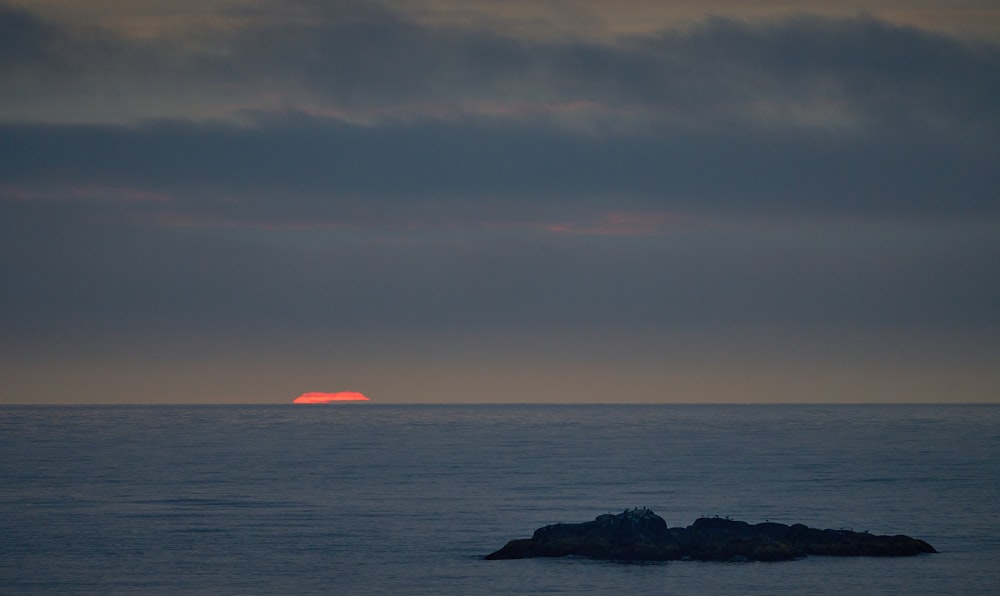 the sun is setting over the ocean with a rock in the foreground