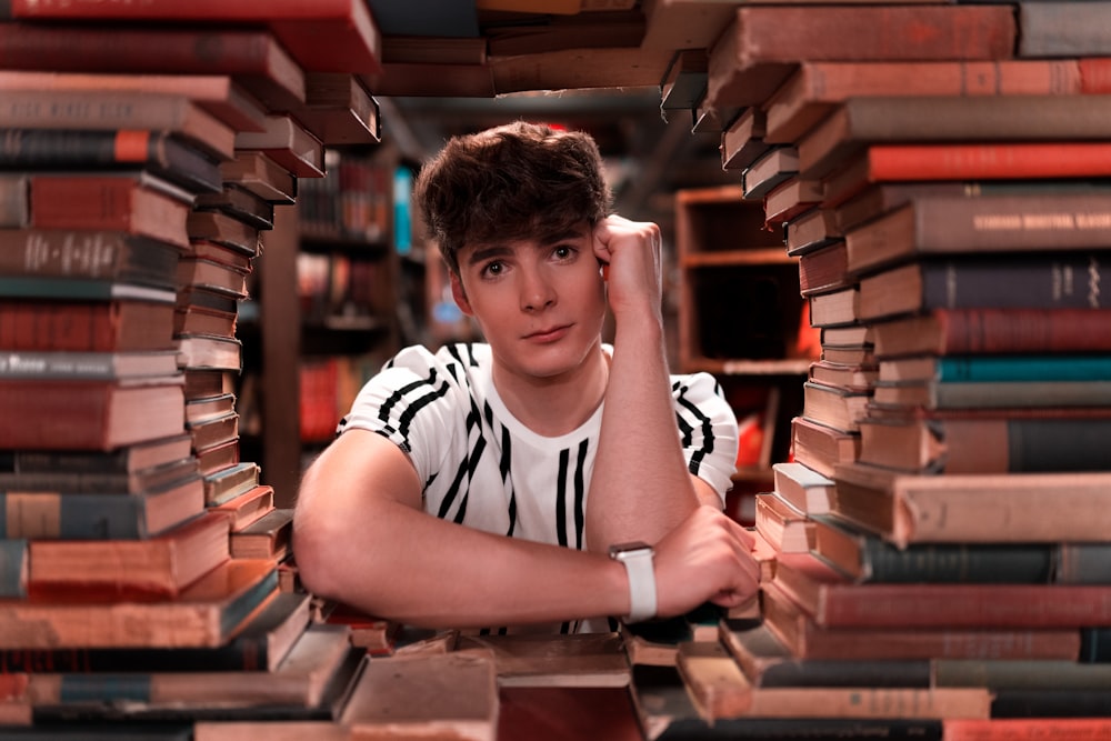 a young man sitting in front of a pile of books
