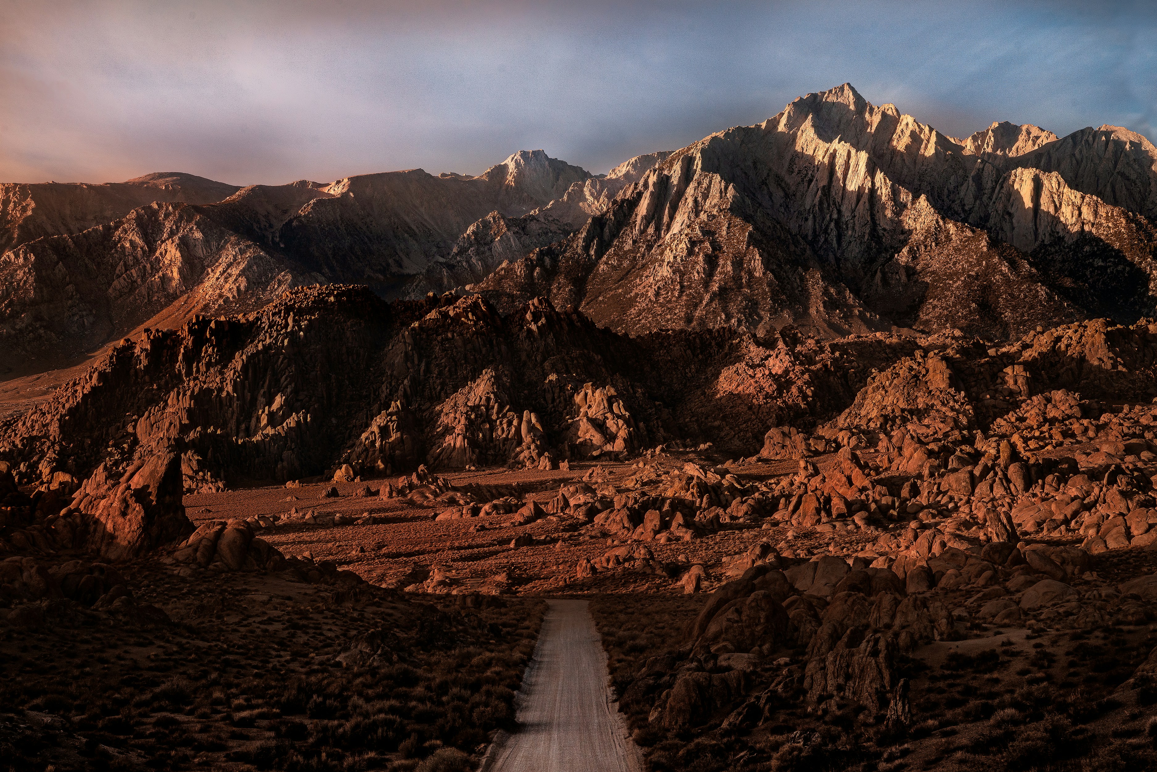 a dirt road surrounded by mountains under a cloudy sky